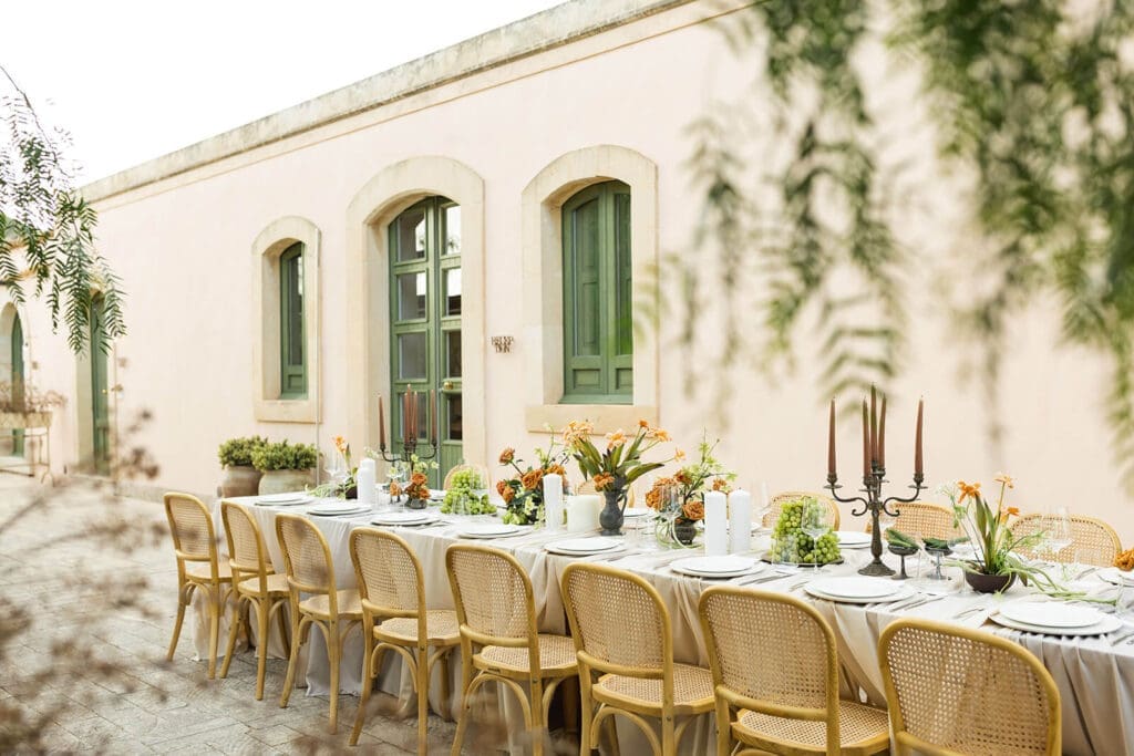Destination wedding outdoor dining table set against a peach-coloured wall at Braccialieri, a 19th-century estate near Noto in southeastern Sicily