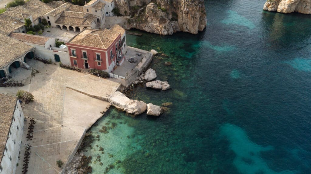 Aerial view of Tonnara di Scopello, a coastal destination wedding venue with limestone faraglioni and turquoise water on the northwest coast of Sicily